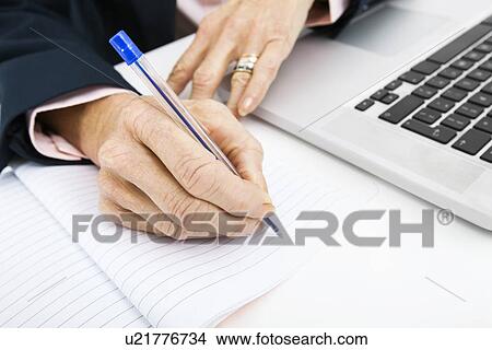 Cropped image of businesswoman with laptop writing in book on office desk View Large Photo Image Picture - Cropped image of businesswoman with laptop writing in book on office desk. Fotosearch