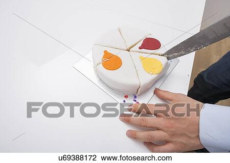Stock Image - Cropped image of man cutting birthday cake at table. Fotosearch
