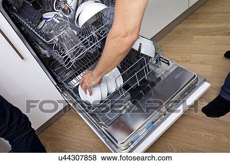 Stock Photo - Cropped image of man loading dishwasher in kitchen. Fotosearch