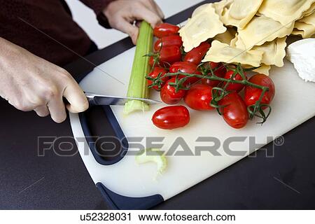 Stock Image - Cropped image of woman chopping cucumber at kitchen counter. Fotosearch