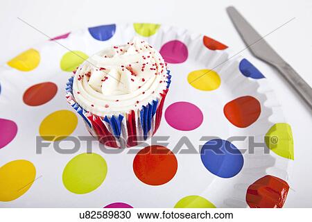 Stock Image - Cupcake in multicolored plate with polka dots against white background. Fotosearch