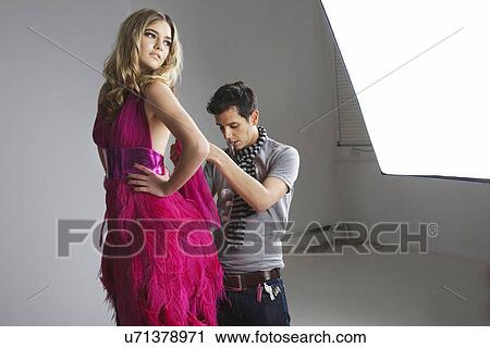 Stock Image - Designer adjusting dress on fashion model in studio. Fotosearch