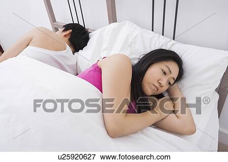 Displeased Asian woman with man sleeping in bed View Large Photo Image Stock Photo - Displeased Asian woman with man sleeping in bed. Fotosearch
