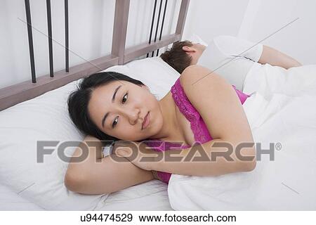 Stock Photo - Displeased woman with man sleeping in bed. Fotosearch