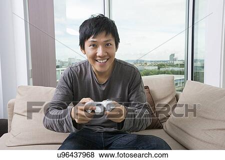 Stock Photo - Excited mid adult man playing video game on sofa. Fotosearch
