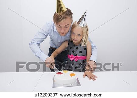 Stock Photo - Father and daughter cutting birthday cake at table. Fotosearch