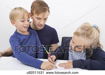 Stock Image - Father and son looking at girl studying at table. Fotosearch