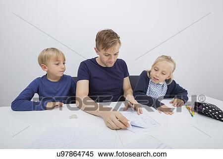 Stock Photography - Father checking children's homework at table. Fotosearch