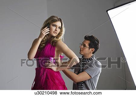 Female fashion model using cell phone while designer adjusting her dress in studio View Large Photo Image Stock Photo - Female fashion model using cell phone while designer adjusting her dress in studio. Fotosearch