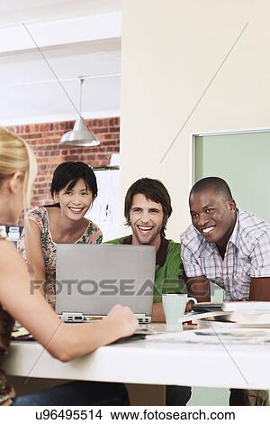 Four people having meeting around laptop laughing. View Large Photo Image Picture - Four people having meeting around laptop laughing.. Fotosearch