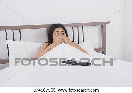 Stock Image - Frightened woman watching TV in bed. Fotosearch