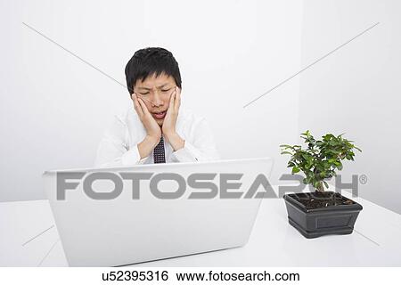Stock Photograph - Frustrated businessman looking at laptop in office. Fotosearch