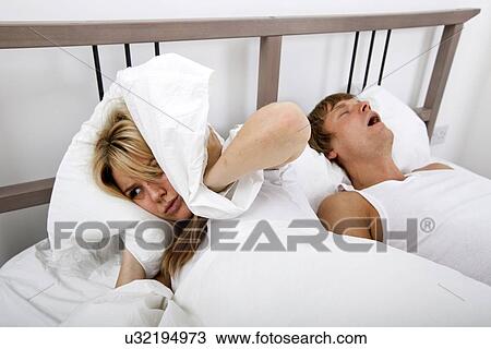 Frustrated woman covering ears with pillow while man snoring in bed View Large Photo Image Stock Image - Frustrated woman covering ears with pillow while man snoring in bed. Fotosearch