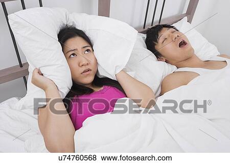 Frustrated woman covering ears with pillow while man snoring in bed View Large Photo Image Stock Photo - Frustrated woman covering ears with pillow while man snoring in bed. Fotosearch