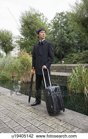 Full length of Asian businessman with luggage standing by pond View Large Photo Image Stock Image - Full length of Asian businessman with luggage standing by pond. Fotosearch