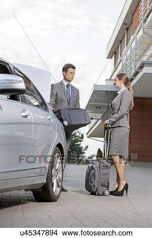 Picture - Full-length of business couple with luggage outside hotel. Fotosearch