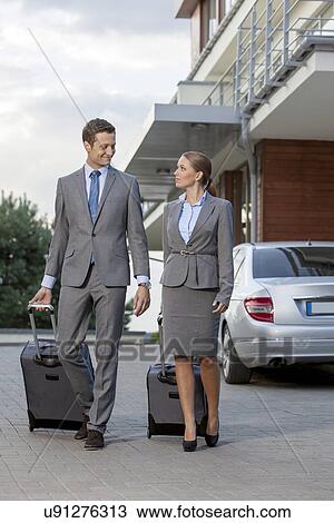 Full-length of business couple with luggage walking outside hotel View Large Photo Image Stock Image - Full-length of business couple with luggage walking outside hotel. Fotosearch