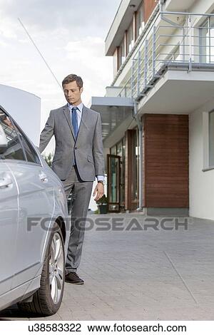 Full-length of businessman standing by car outside hotel View Large Photo Image Stock Image - Full-length of businessman standing by car outside hotel. Fotosearch