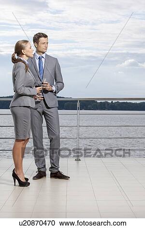 Stock Image - Full length of businesspeople holding wineglasses on terrace. Fotosearch