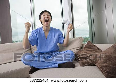 Full length of excited mid adult man playing video game in living room View Large Photo Image Stock Image - Full length of excited mid adult man playing video game in living room. Fotosearch