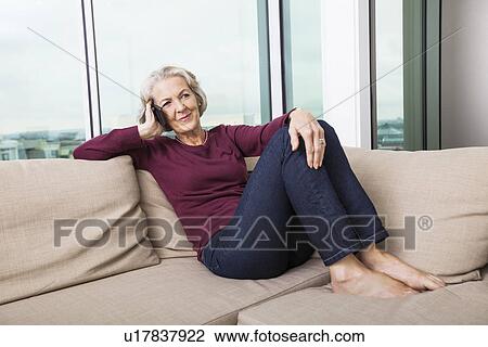 Full-length of senior woman answering smart phone on sofa at home View Large Photo Image Stock Image - Full-length of senior woman answering smart phone on sofa at home. Fotosearch