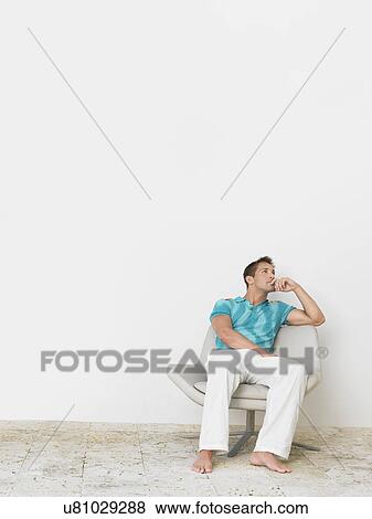 Stock Photo - Full length of thoughtful young man sitting on chair. Fotosearch