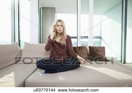 Full length of young displeased woman talking on mobile phone at home View Large Photo Image Picture - Full length of young displeased woman talking on mobile phone at home. Fotosearch
