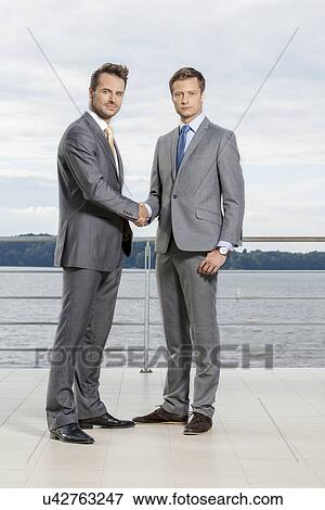 Stock Photo - Full length portrait of businessmen shaking hands on terrace. Fotosearch