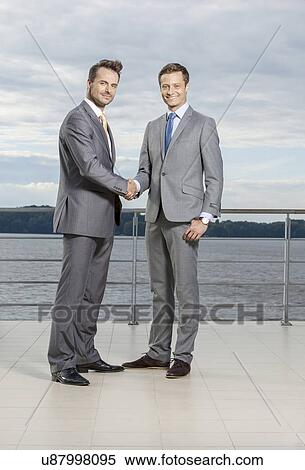 Stock Photography - Full length portrait of businessmen shaking hands on terrace. Fotosearch