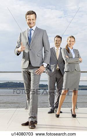Full length portrait of confident businessman gesturing thumbs up while standing with coworkers on terrace against sky View Large Photo Image Stock Image - Full length portrait of confident businessman gesturing thumbs up while standing with coworkers on terrace against sky. Fotosearch
