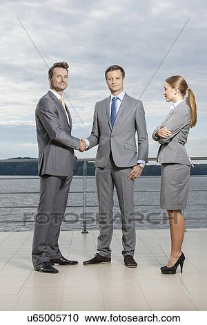 Full length portrait of young businessmen shaking hands while businesswoman looking at them on terrace View Large Photo Image Stock Image - Full length portrait of young businessmen shaking hands while businesswoman looking at them on terrace. Fotosearch