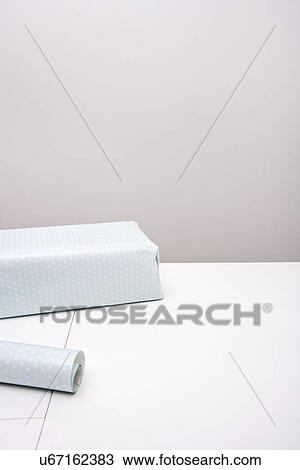 Stock Image - Gift box and wrapping paper on table against gray background. Fotosearch