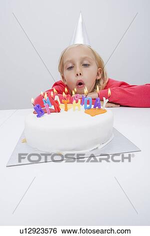 Girl blowing candles on birthday cake at table in house View Large Photo Image Stock Photograph - Girl blowing candles on birthday cake at table in house. Fotosearch