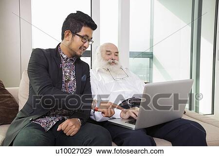 Stock Photo - Grandfather and grandson using laptop in living room. Fotosearch