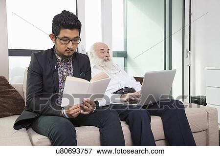 Grandson reading book while grandfather using laptop on sofa at home View Large Photo Image Stock Photo - Grandson reading book while grandfather using laptop on sofa at home. Fotosearch