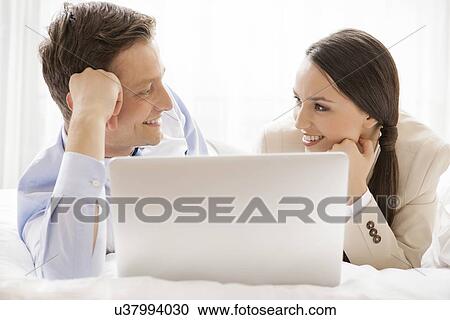 Happy business couple with laptop looking at each other in hotel View Large Photo Image Stock Image - Happy business couple with laptop looking at each other in hotel. Fotosearch