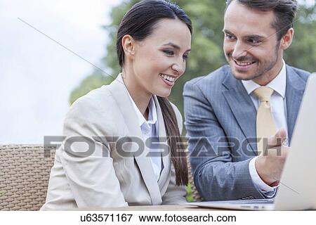 Stock Photo - Happy businesspeople discussing over laptop outdoors. Fotosearch