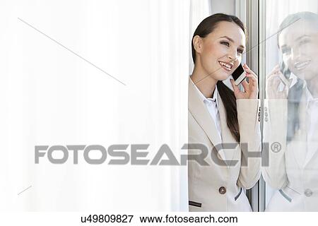 Happy businesswoman answering cell phone in office View Large Photo Image Stock Photo - Happy businesswoman answering cell phone in office. Fotosearch