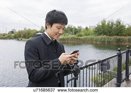 Happy mid adult businessman text messaging through mobile phone at bridge railing View Large Photo Image Stock Photo - Happy mid adult businessman text messaging through mobile phone at bridge railing. Fotosearch