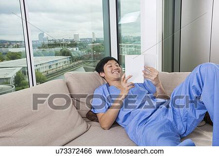 Happy mid adult man reading book while lying on sofa by window View Large Photo Image Stock Photograph - Happy mid adult man reading book while lying on sofa by window. Fotosearch