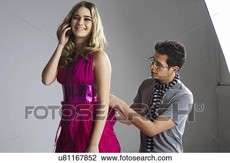 Happy model using cell phone while male designer adjusting her dress in studio View Large Photo Image Stock Image - Happy model using cell phone while male designer adjusting her dress in studio. Fotosearch