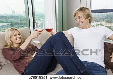 Stock Image - Happy relaxed couple toasting wine glasses in living room at home. Fotosearch