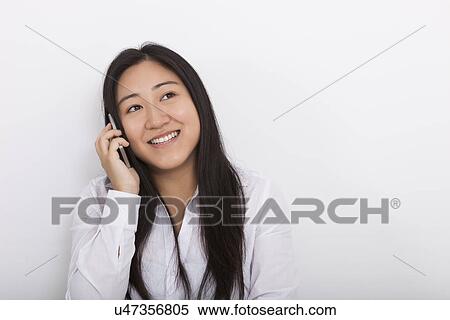 Stock Photography - Happy woman answering cell phone against white background. Fotosearch