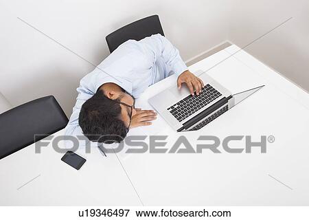 High angle view of businessman sleeping by laptop at desk in office View Large Photo Image Stock Photo - High angle view of businessman sleeping by laptop at desk in office. Fotosearch