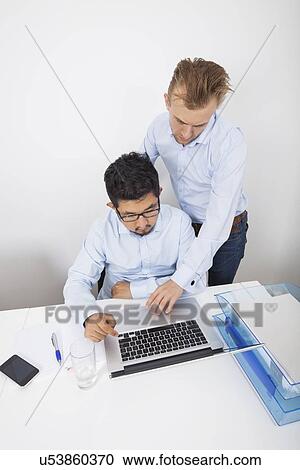 Stock Image - High angle view of businessmen using laptop in office. Fotosearch