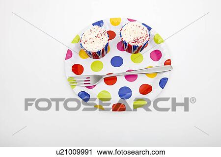 Stock Image - High angle view of cupcakes in multicolored plate against white background. Fotosearch