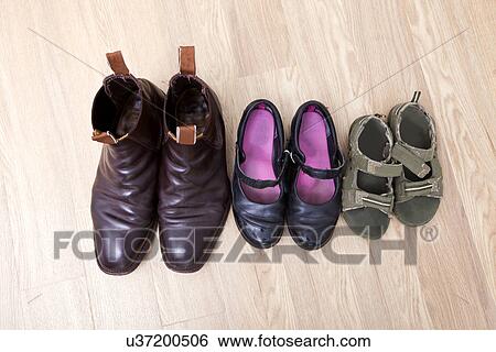 Stock Photograph - High angle view of family shoes placed in a row on hardwood floor. Fotosearch