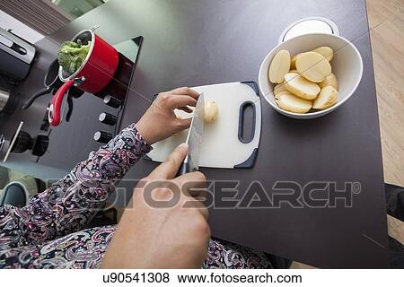 Stock Photo - High angle view of man cutting potato at kitchen counter. Fotosearch