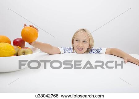 Little girl holding orange from fruit bowl at table View Large Photo Image Stock Photograph - Little girl holding orange from fruit bowl at table. Fotosearch
