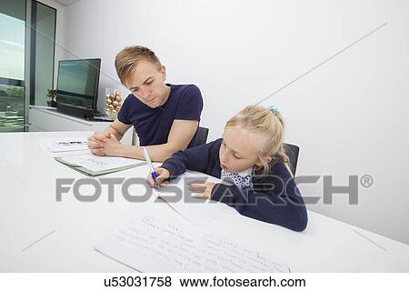 Stock Photo - Little girl studying while sitting by father at table. Fotosearch